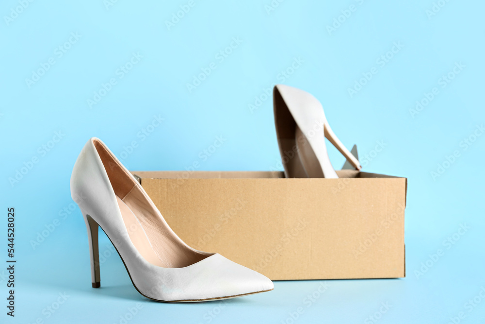 Cardboard box with white high-heeled shoes on blue background