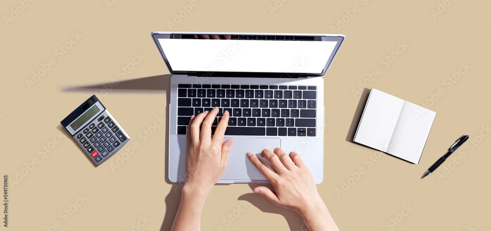 Person using a laptop computer with a notebook and a calculator - flat lay