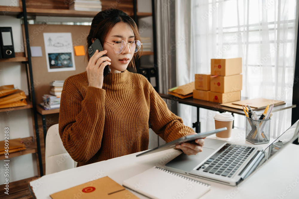 Portrait of Asian young woman SME working using smartphone or tablet taking receive and checking onl