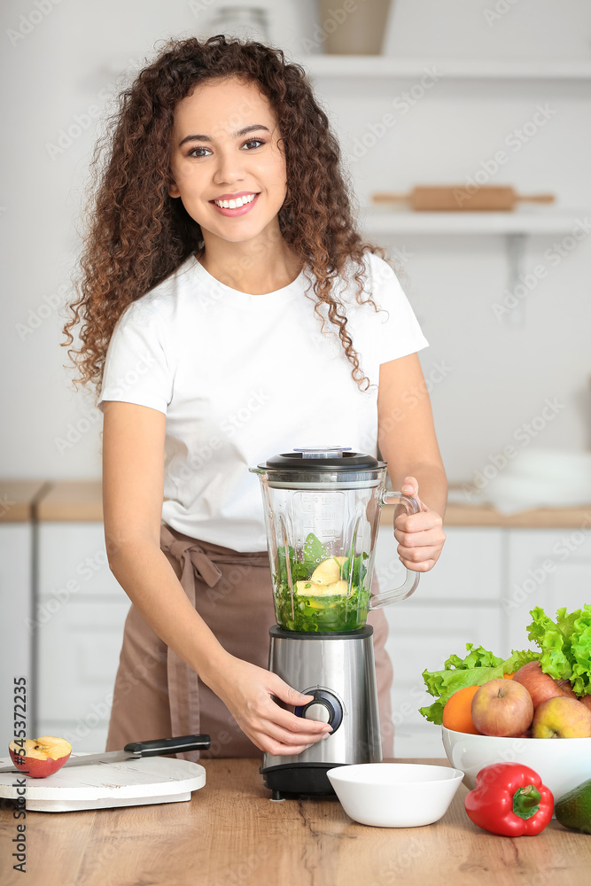 Young African-American woman making healthy smoothie in kitchen