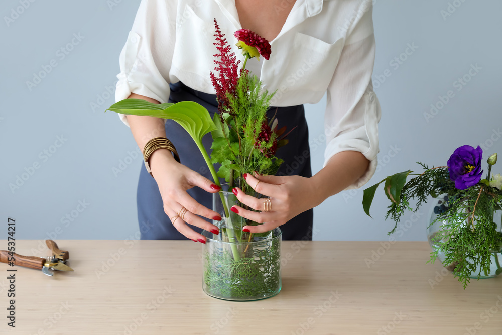 年轻女子在灰色墙壁附近的桌子旁制作美丽的插花