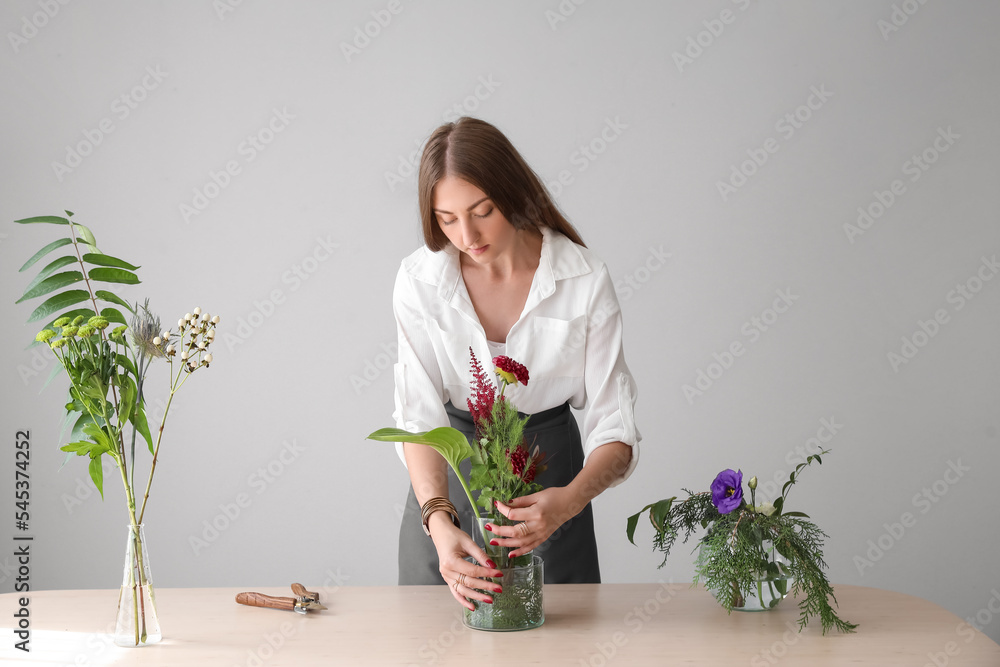 年轻女子在灰色墙壁附近的桌子旁制作美丽的插花