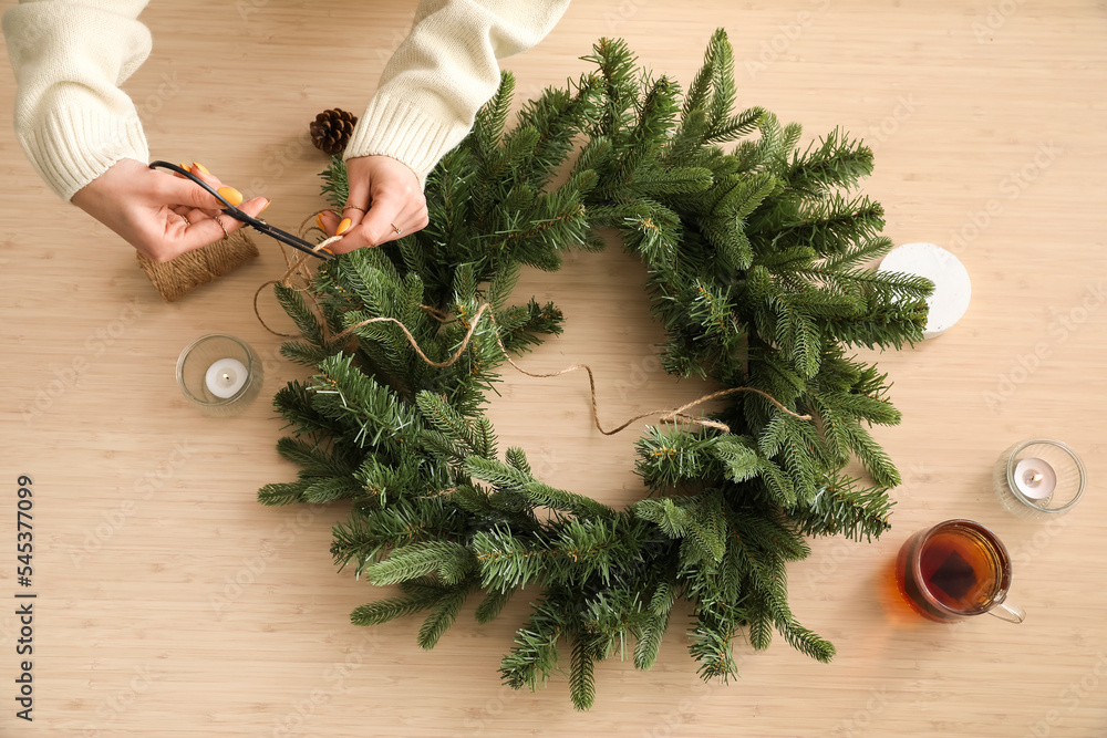 Woman cutting rope for Christmas wreath on wooden background