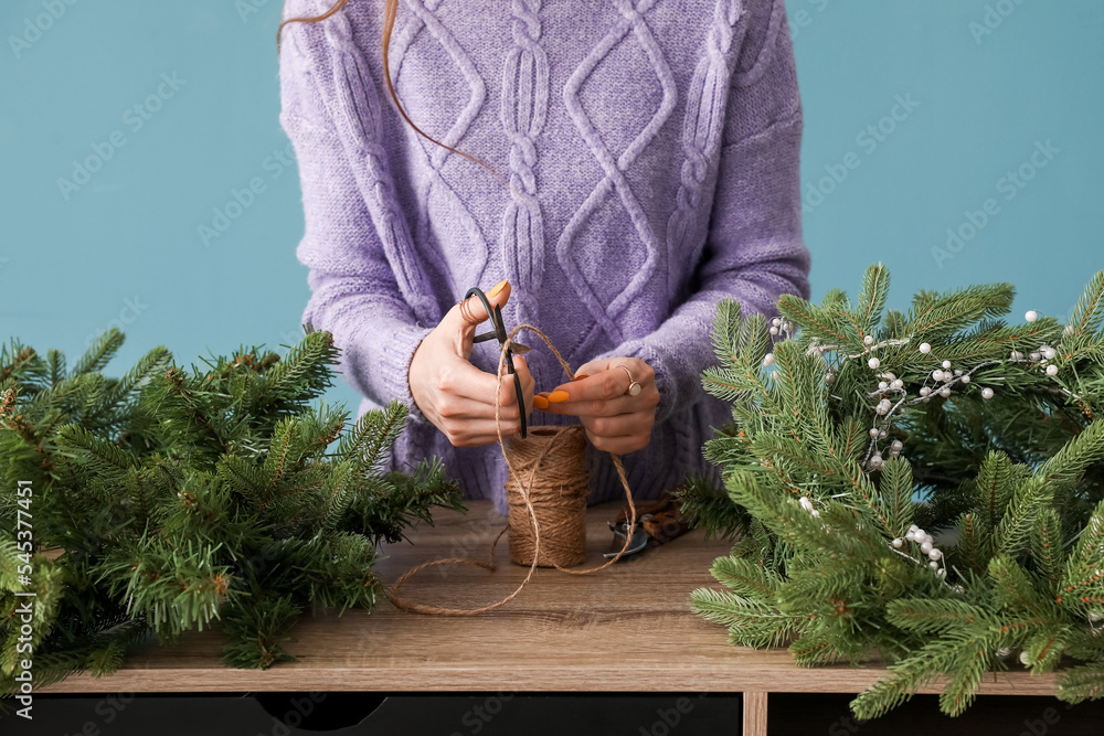 Woman making Christmas wreath at wooden table near blue wall, closeup