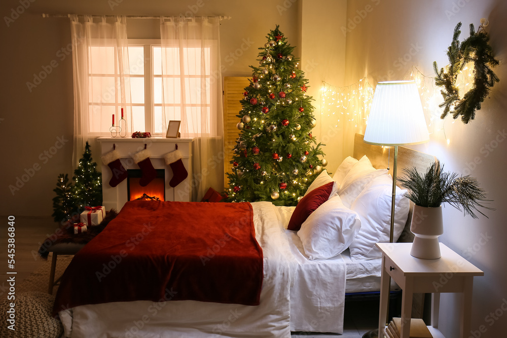 Interior of bedroom with glowing Christmas trees and fireplace