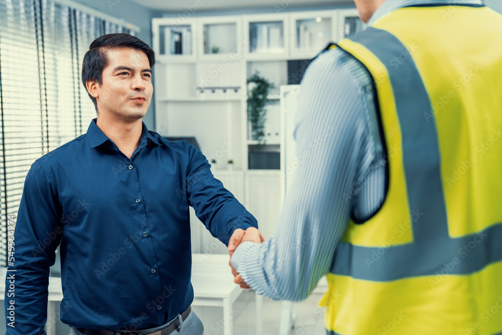 An engineer with a protective vest handshake with an investor in his office. Following a successful 