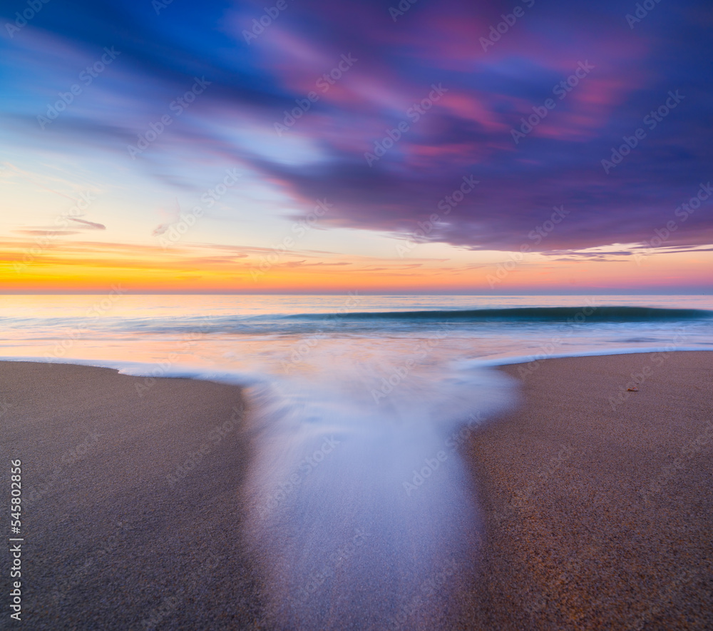 A seascape during sunset. Sand on the seashore. Bright sky during sunset. A sandy beach at low tide.