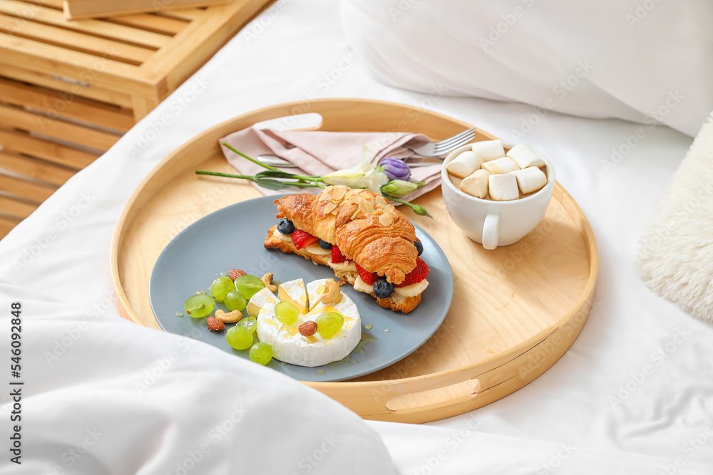 Wooden tray with tasty breakfast and cup of cacao on bed