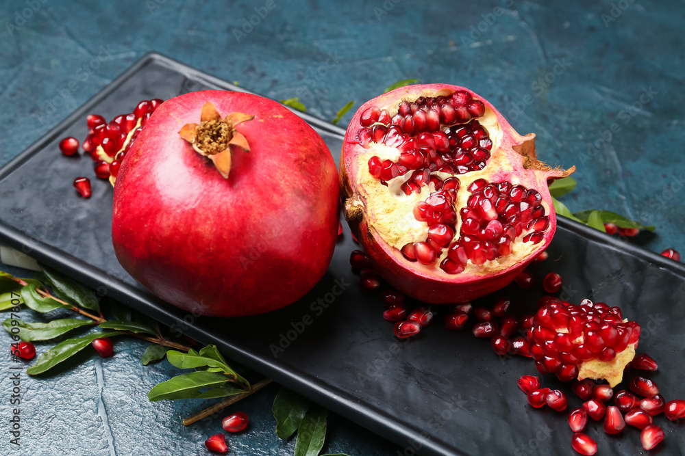 Board with fresh pomegranates on dark color background, closeup