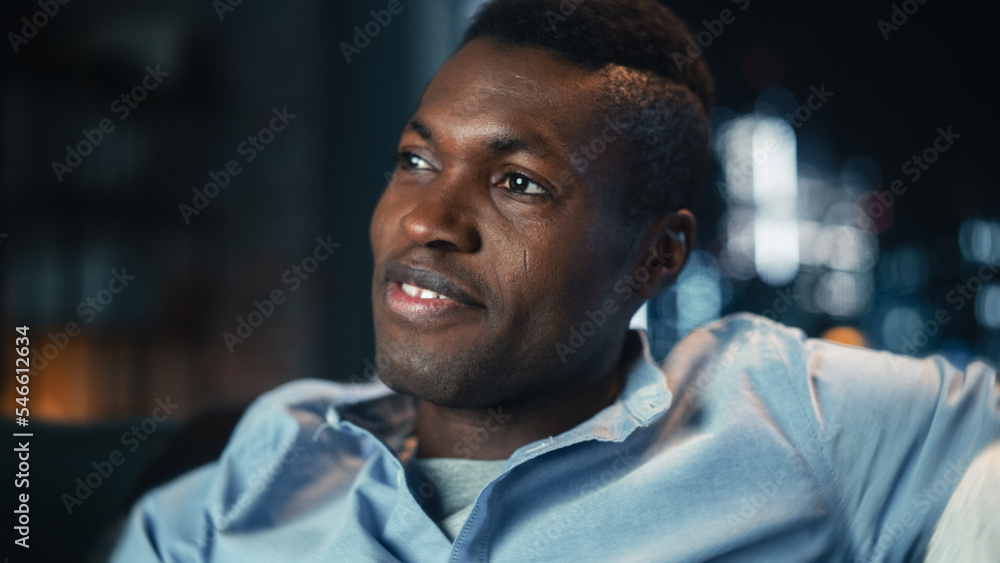 Portrait of a Handsome Black Man Sitting on a Couch at Home at Night, Watching Comedy Series on TV i