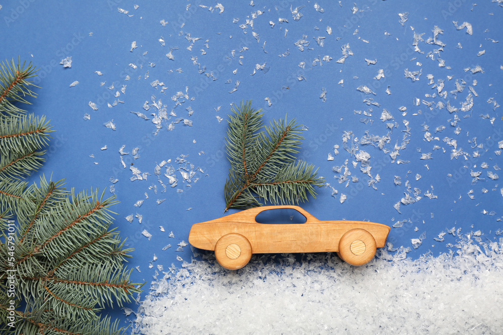 Toy car with Christmas branches and snow on blue background