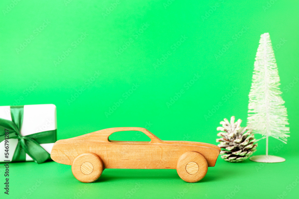 Toy car with Christmas tree, fir cone and gift on green background