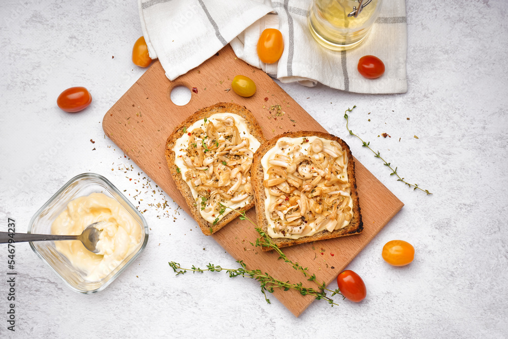 Wooden board of tasty toasts with cream cheese, mushrooms and tomatoes on light background