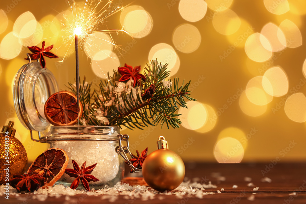 Jar with Christmas sparkler, fir branches and decor on table against blurred lights