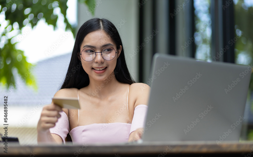 有魅力的亚洲女人拿着信用卡，用笔记本电脑在网上购物。