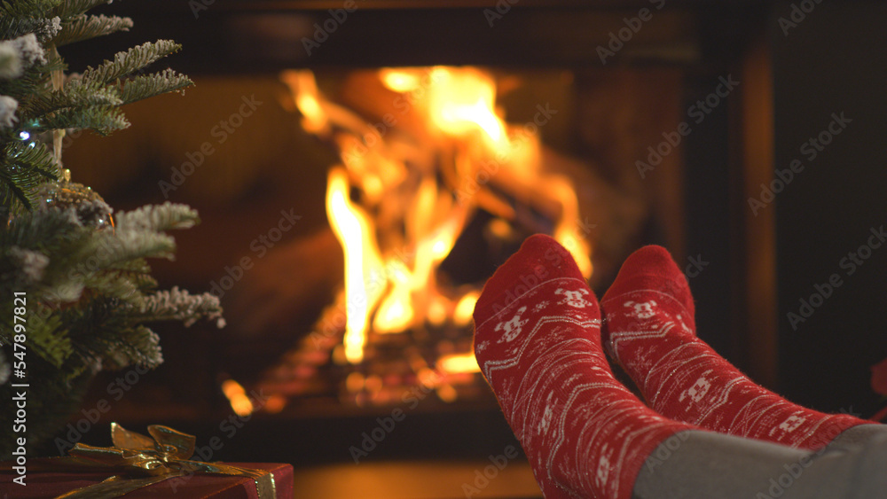 CLOSE UP: Woman warming up her feet in Christmas socks and relaxing by fireplace