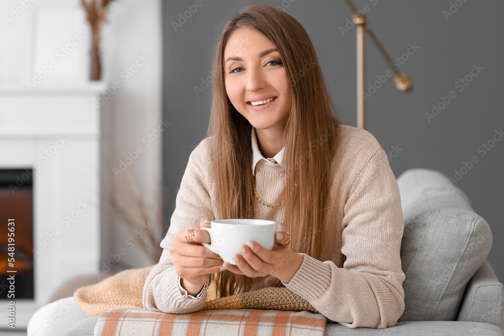 坐在家里沙发上拿着一杯热饮料的年轻女人