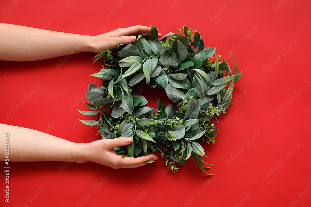 Female hands with stylish Christmas wreath on red background