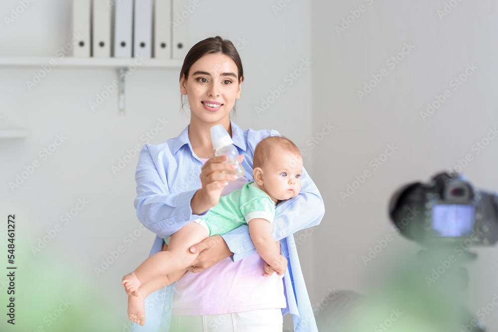 Young woman with baby and bottle recording video course at home