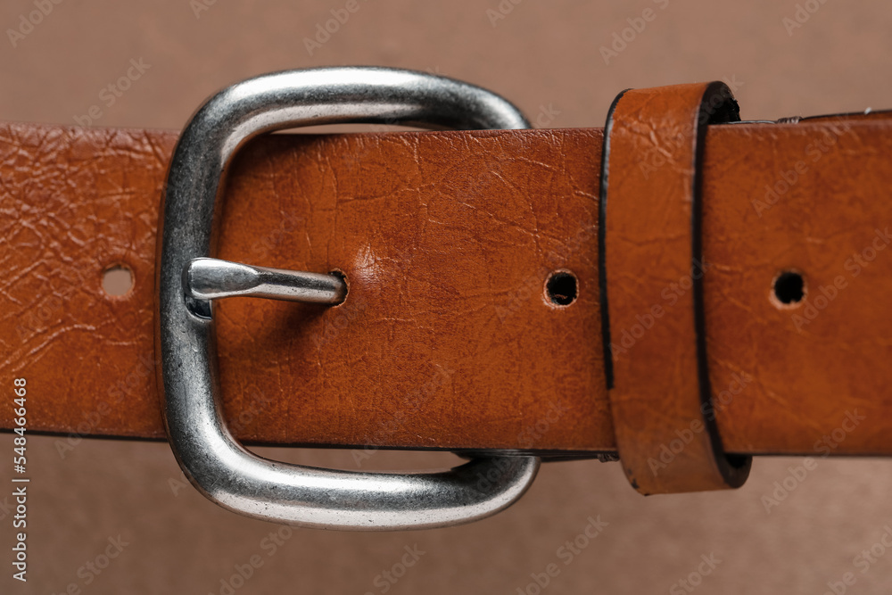 Closeup view of leather belt with metal buckle on brown background