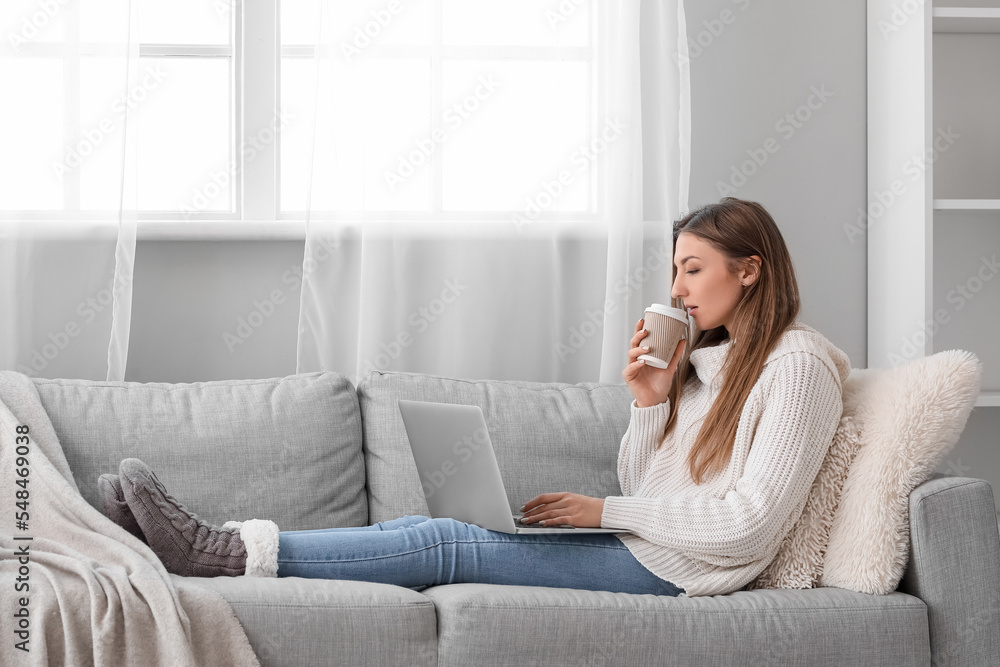 年轻女人在家里用笔记本电脑喝咖啡