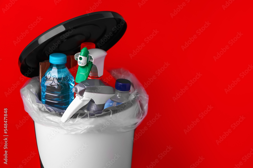 Open rubbish bin with cleaning supplies on red background