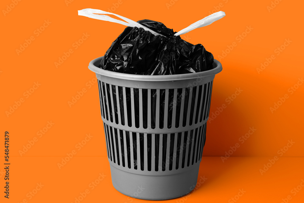 Bag with garbage in rubbish bin on color background