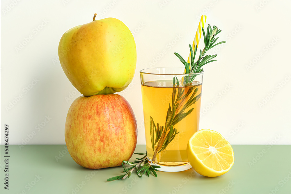 Ripe apples and glass of fresh juice with rosemary on color table