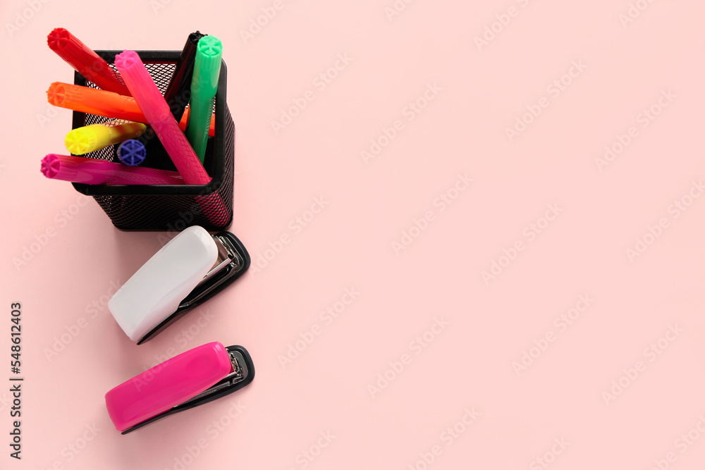 Holder with felt-tip pens and staplers on pink background