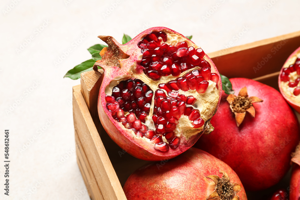 Wooden box with fresh pomegranates on light background, closeup