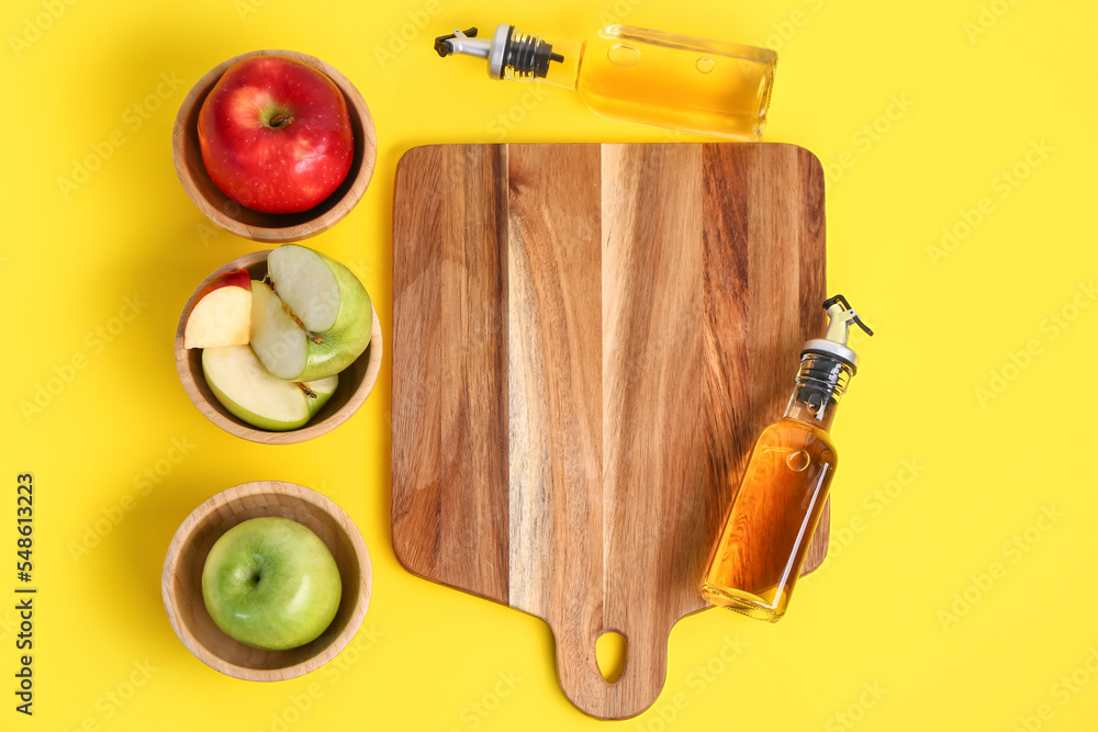 Composition with bottles of apple cider vinegar, fruits and wooden board on yellow background