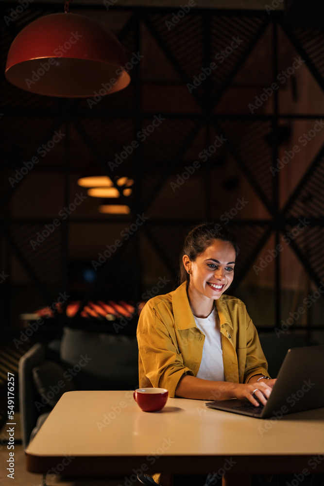 Smiling businesswoman typing over the laptop, working late at night, at the office.