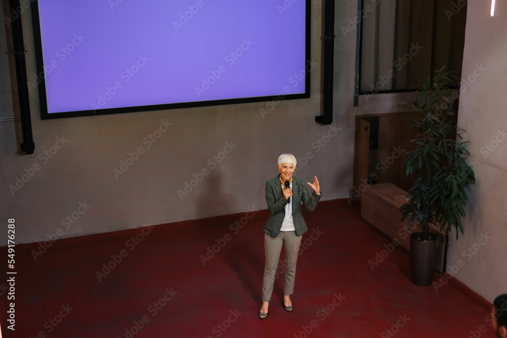 Mature woman giving a lecture, holding and talking over the microphone.