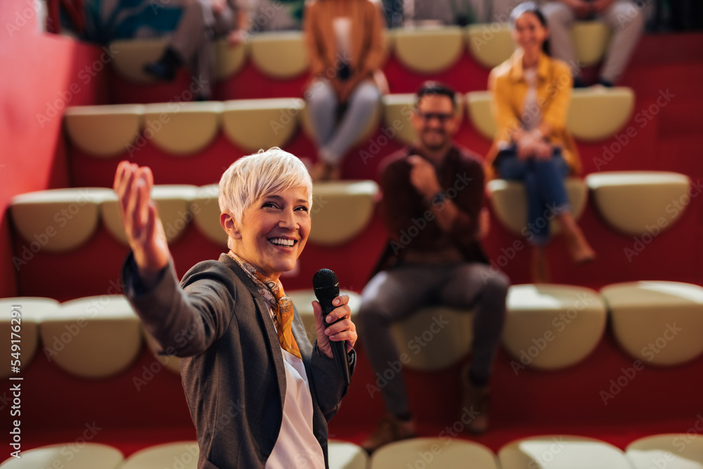 Businesswoman giving the lecture to her colleagues, using a microphone.