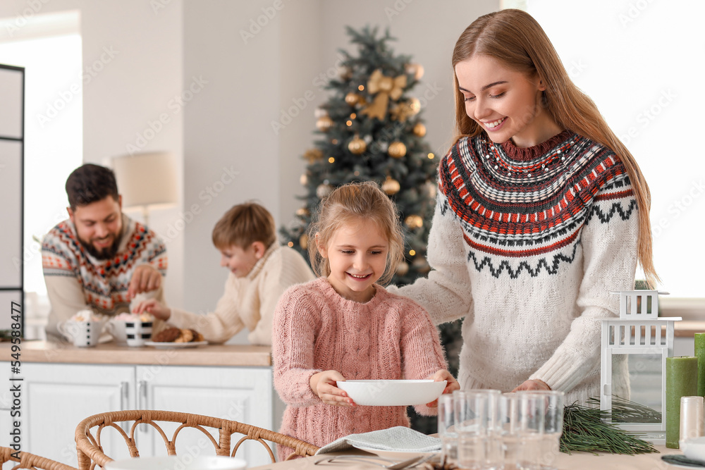 Little girl with her mother setting dining table in kitchen on Christmas eve