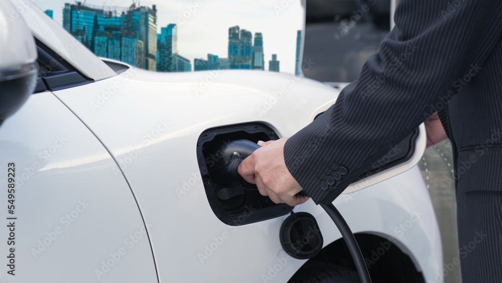 Progressive businessman recharge his electric vehicle with charger cable plug from charging station 