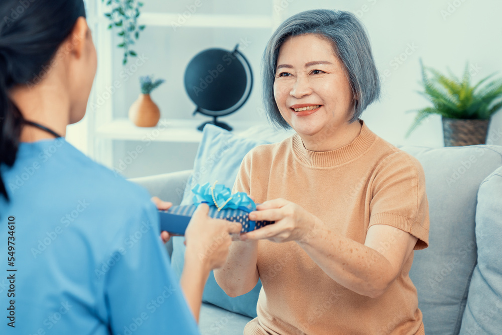 A young caregiver hand over to her senior patient a blue gift box with blue ribbons at a contented l