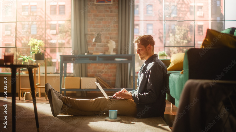 Handsome Young Man Using Laptop, Working from Home Living Room with Big Windows. Male Sitting on Flo