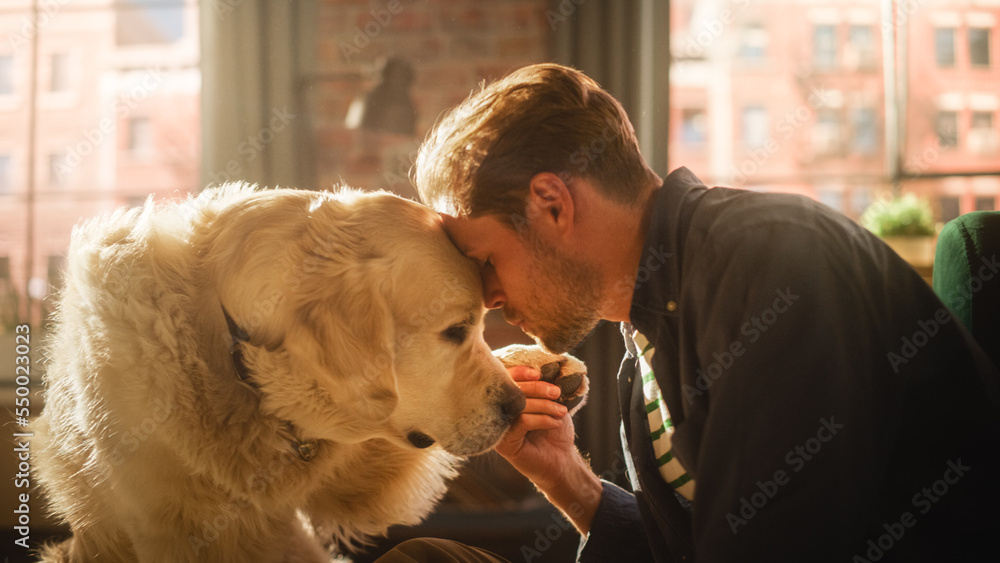 成功的年轻成年男子在家里和他的狗玩耍，活跃的金毛寻回犬。男子坐在F上