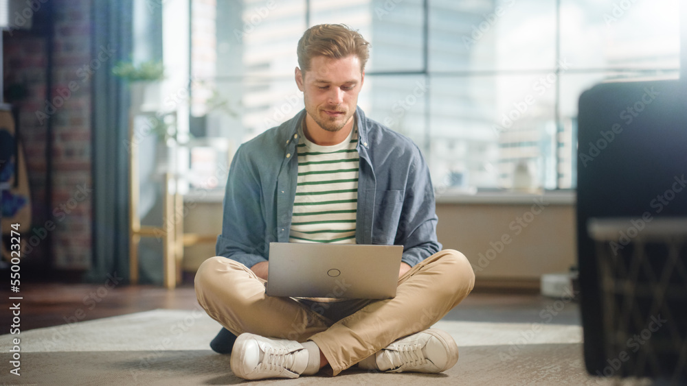 Handsome Young Man Using Laptop, Working from Home Living Room with Big Windows. Male Sitting on Flo