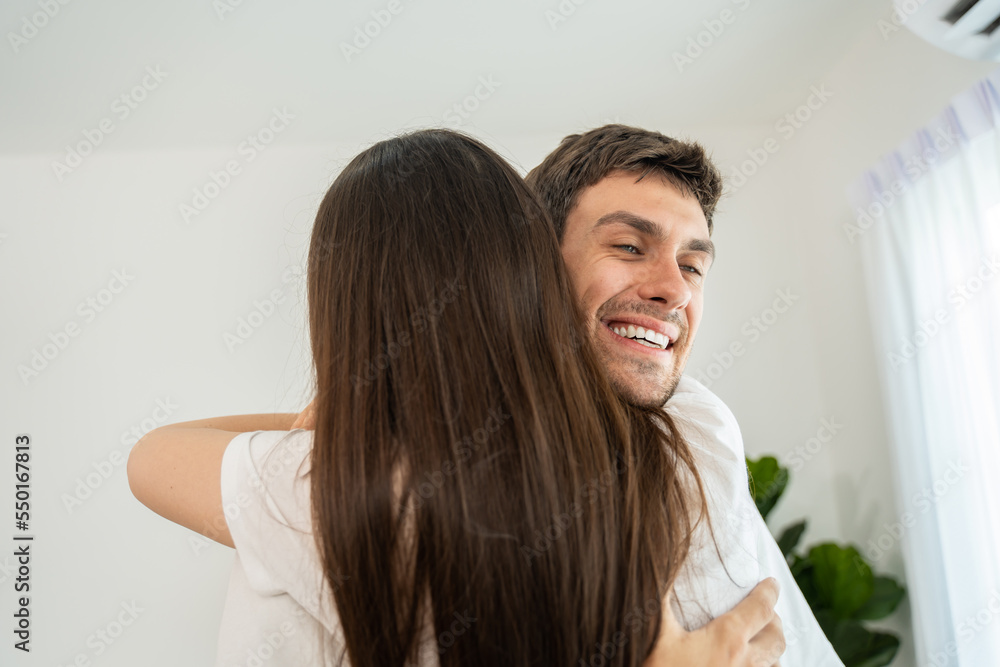 Caucasian young man and woman hugging each other in living room at home. 