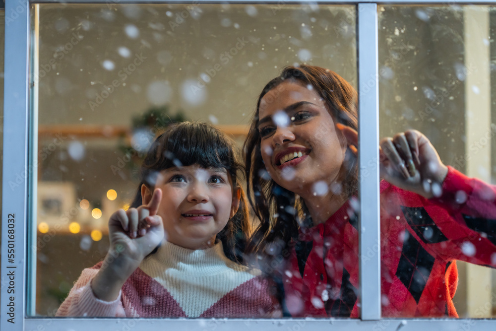 Adorable child looking at the window and admire snowflakes with mother. 