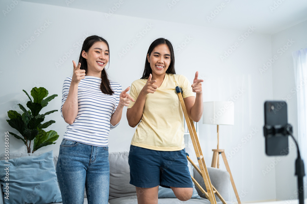 Asian young amputee recording dance with friend in living room at home.