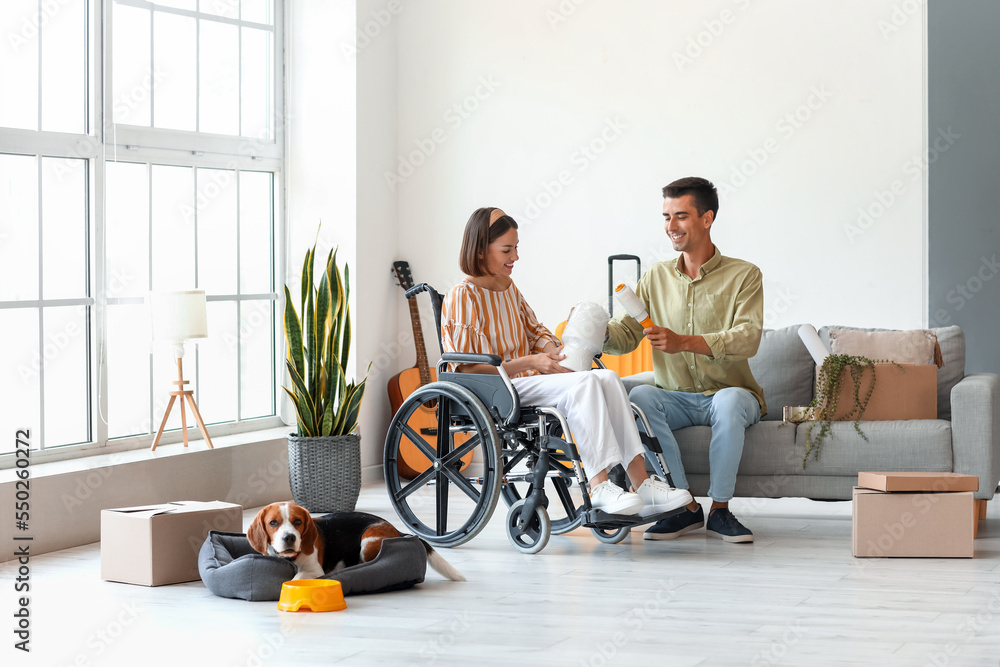 Young man with his wife in wheelchair and dog packing things in room on moving day