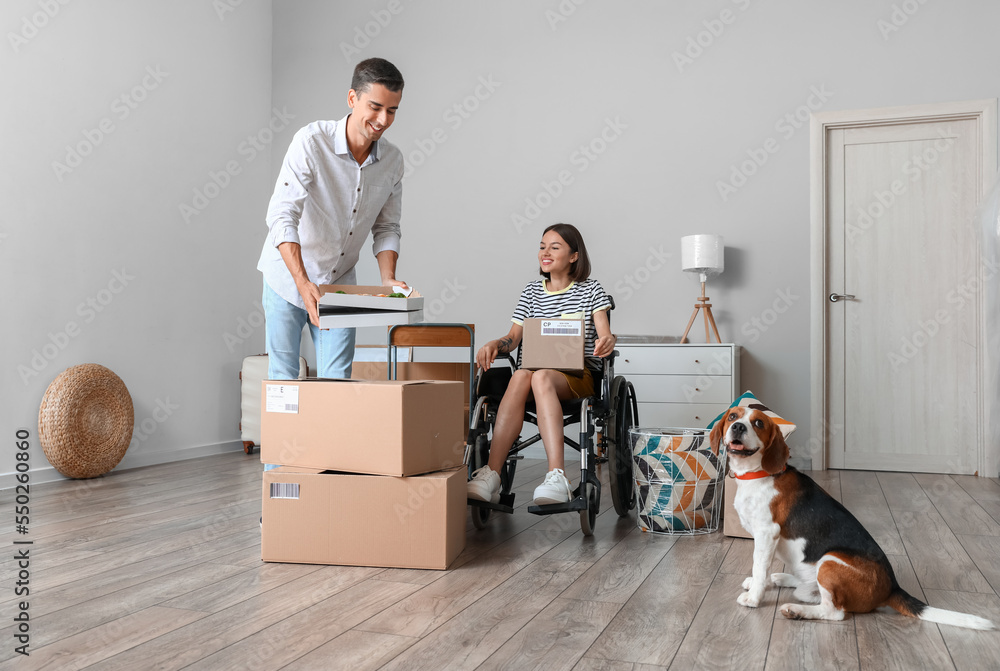 Young man with pizza, his wife in wheelchair and dog in their new flat on moving day