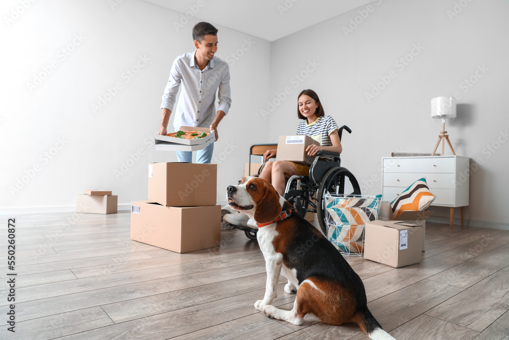 Young man with pizza, his wife in wheelchair and dog in their new flat on moving day