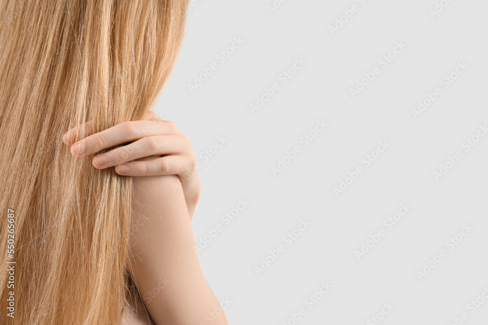 Woman touching blonde hair on light background