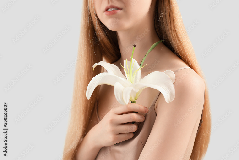 Blonde woman with long hair holding lily flower on light background