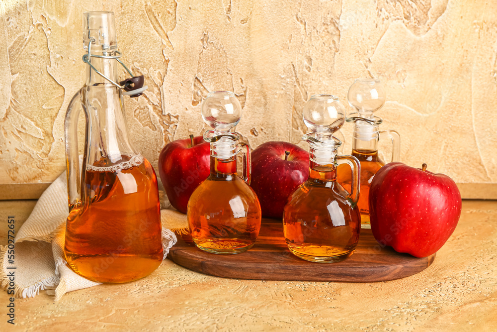 Wooden board with decanters of fresh apple juice and fruits on color table