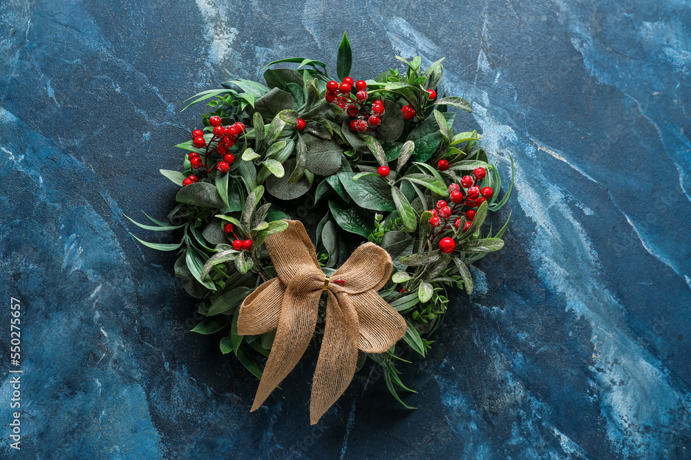 Stylish Christmas wreath decorated with red berries and bow on color background